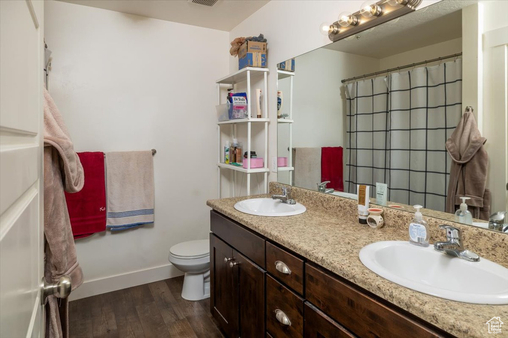 Bathroom with double sink vanity, toilet, and hardwood / wood-style floors