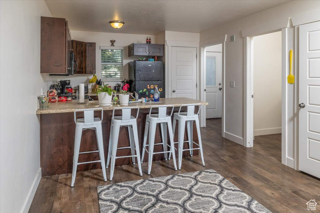 Kitchen with a breakfast bar, dark hardwood / wood-style flooring, black fridge, and dark brown cabinetry