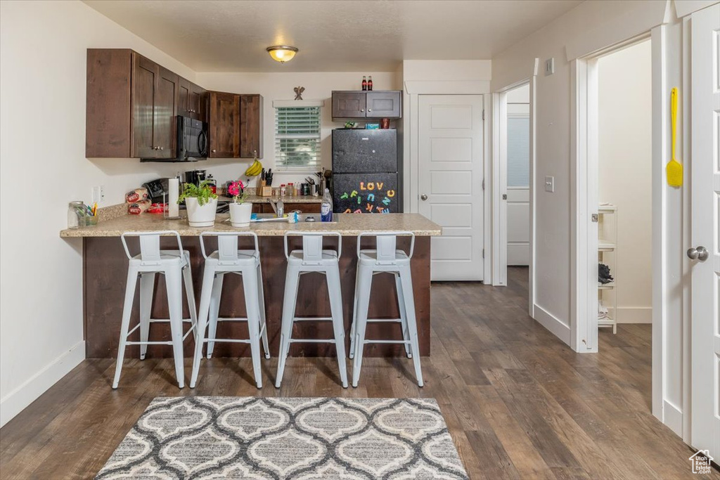 Kitchen with dark brown cabinets, black refrigerator, dark hardwood / wood-style flooring, and a breakfast bar