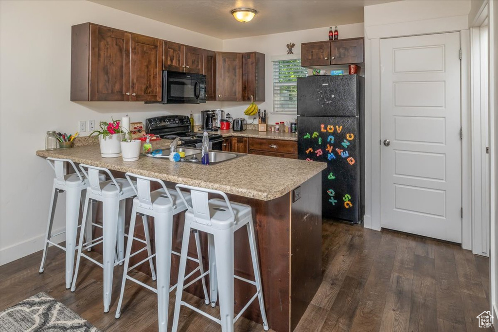 Kitchen featuring black appliances, sink, a kitchen bar, and dark hardwood / wood-style floors