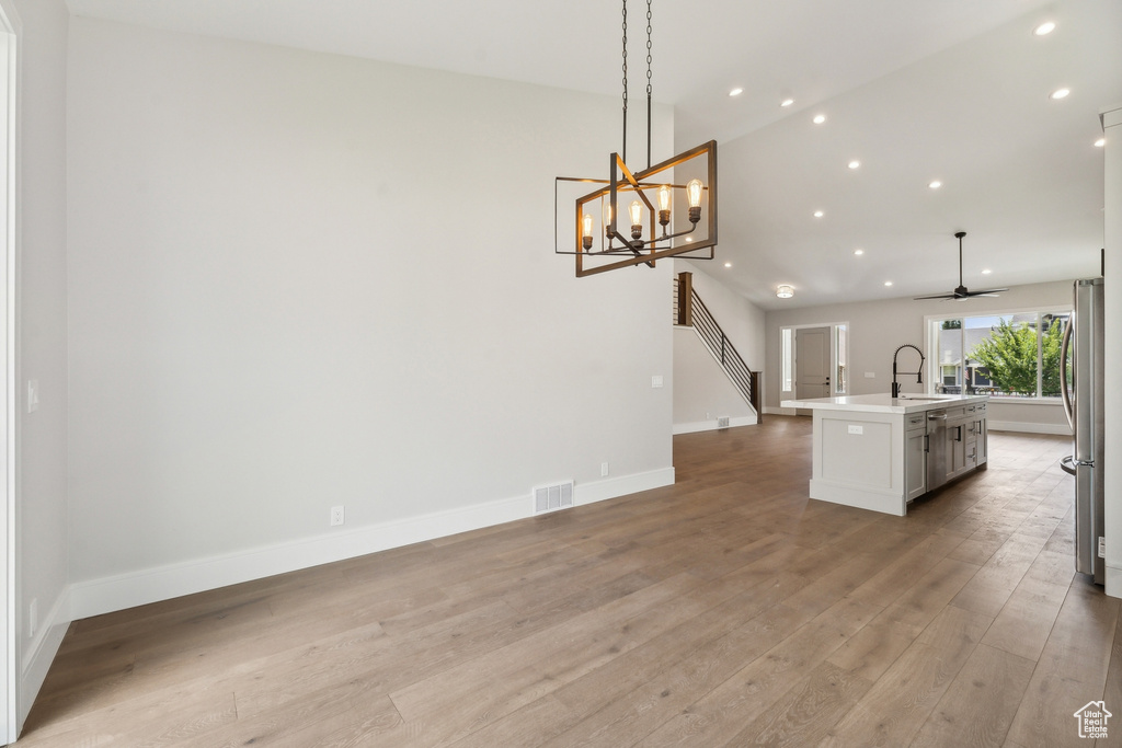 Unfurnished dining area with ceiling fan with notable chandelier, light wood-type flooring, and sink