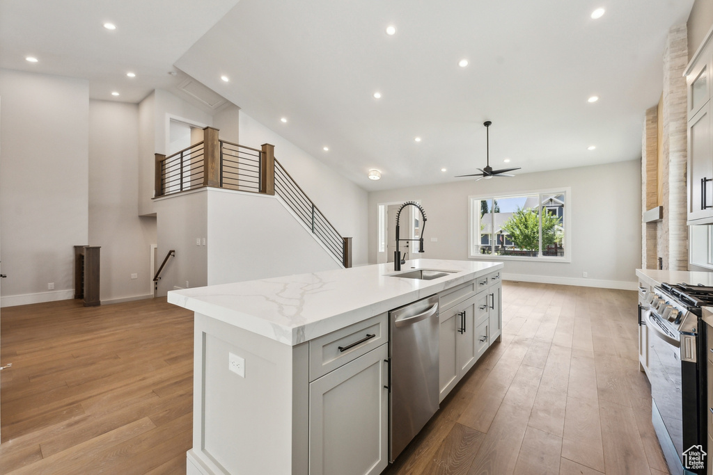 Kitchen featuring stainless steel appliances, an island with sink, light hardwood / wood-style floors, light stone countertops, and sink