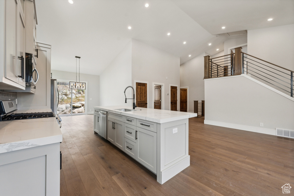 Kitchen with dark wood-type flooring, an island with sink, sink, and hanging light fixtures