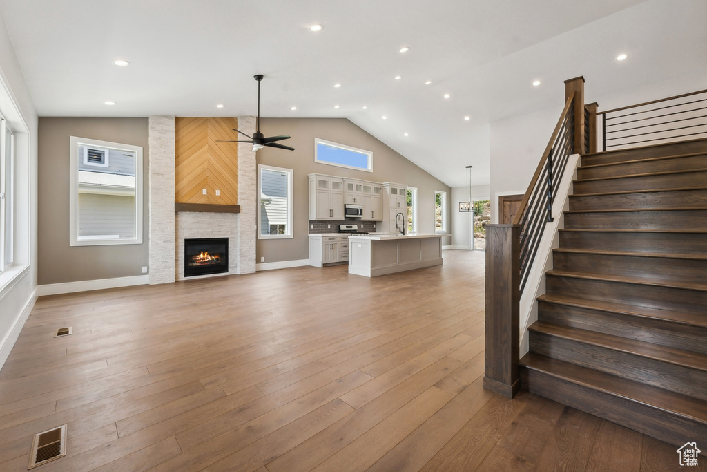 Unfurnished living room with light wood-type flooring, a fireplace, high vaulted ceiling, ceiling fan, and sink