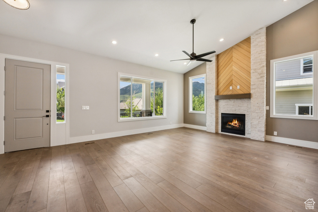 Unfurnished living room with ceiling fan, a stone fireplace, wood-type flooring, and lofted ceiling