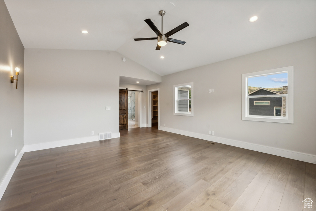 Spare room with ceiling fan, a barn door, hardwood / wood-style flooring, and vaulted ceiling