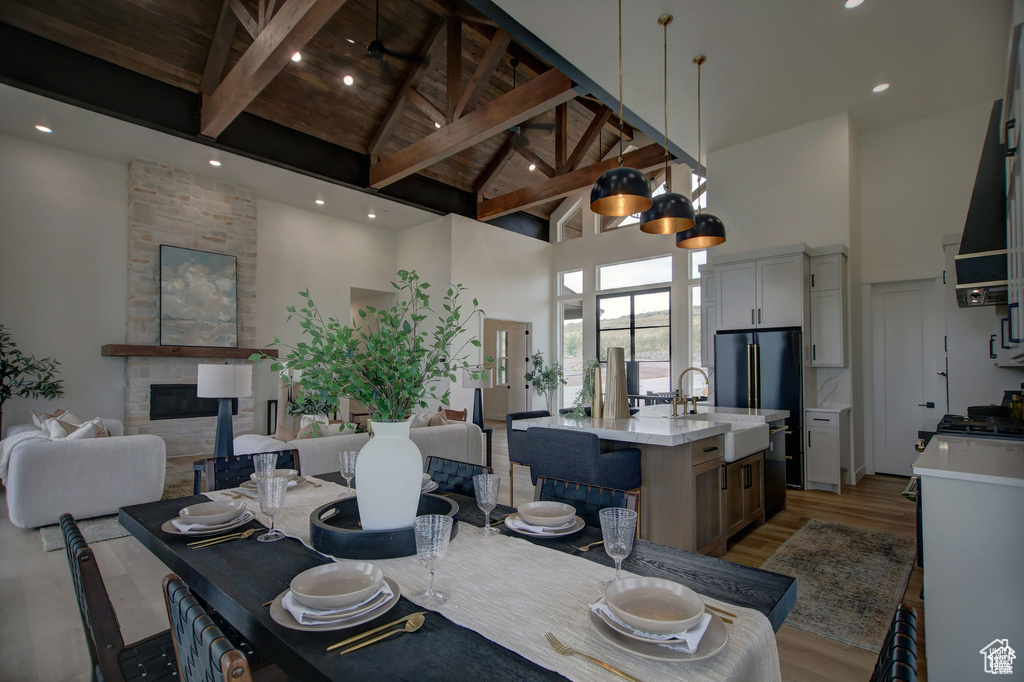 Dining space featuring light hardwood / wood-style flooring, high vaulted ceiling, a fireplace, beamed ceiling, and sink