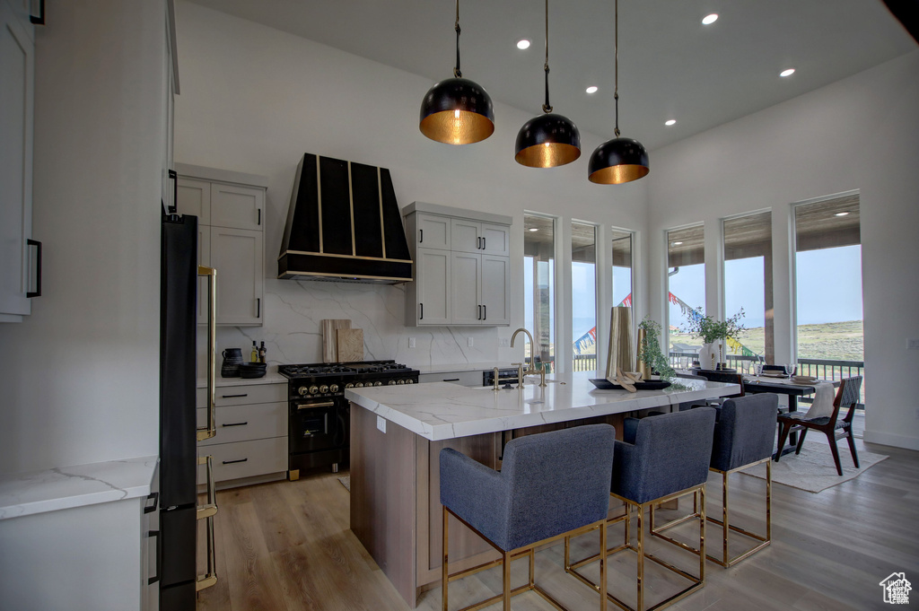 Kitchen featuring decorative backsplash, gas range, light hardwood / wood-style floors, black fridge, and wall chimney exhaust hood