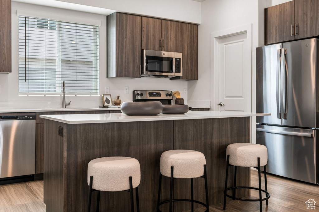 Kitchen featuring light wood-type flooring, stainless steel appliances, a healthy amount of sunlight, a center island, and a kitchen bar