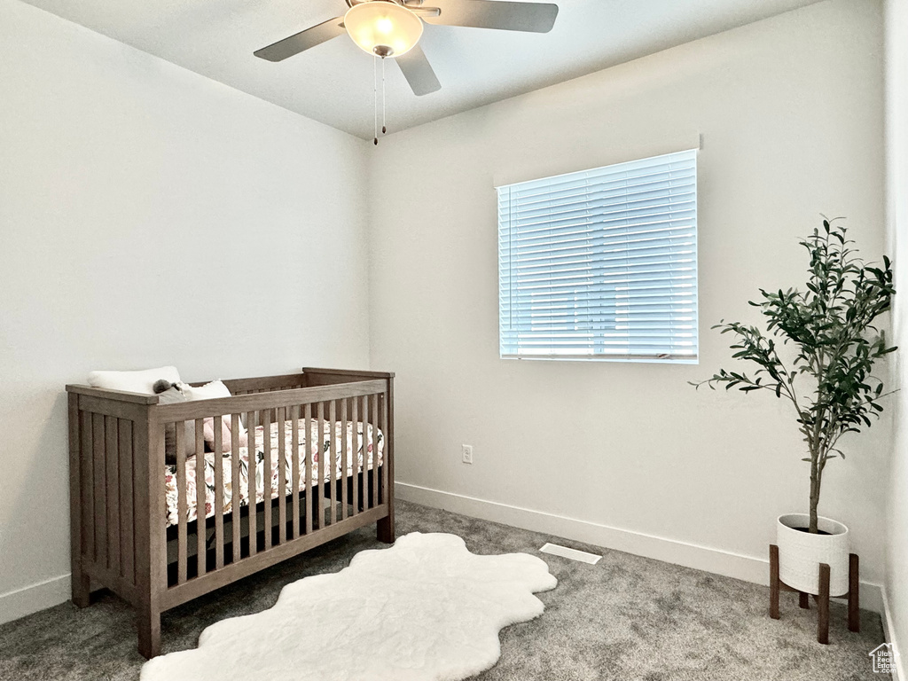 Carpeted bedroom featuring ceiling fan and a crib