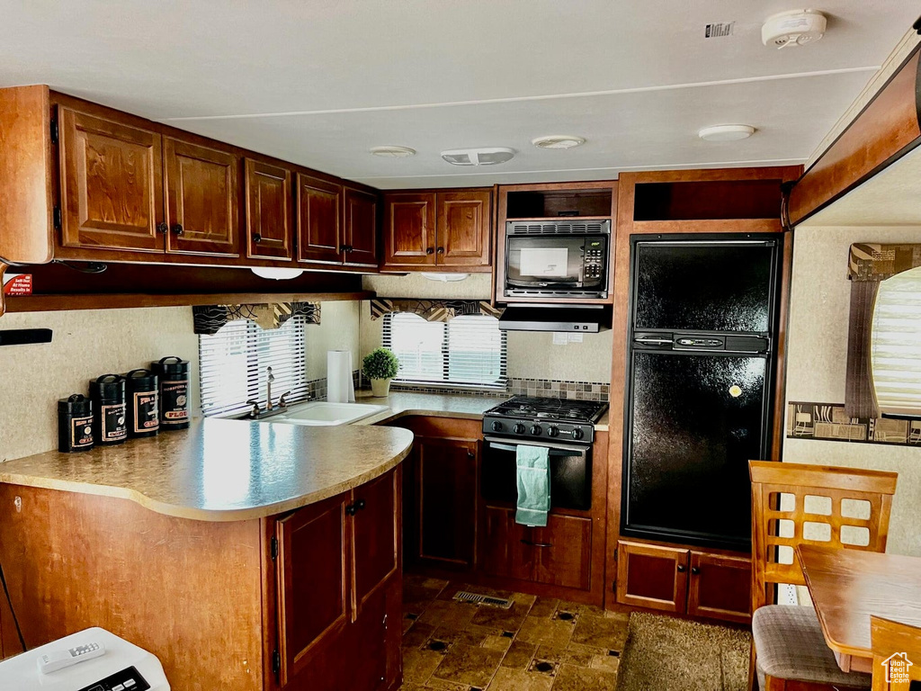 Kitchen with dark tile patterned flooring, black appliances, sink, and kitchen peninsula