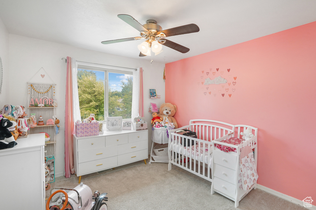 Bedroom featuring light colored carpet, a crib, and ceiling fan