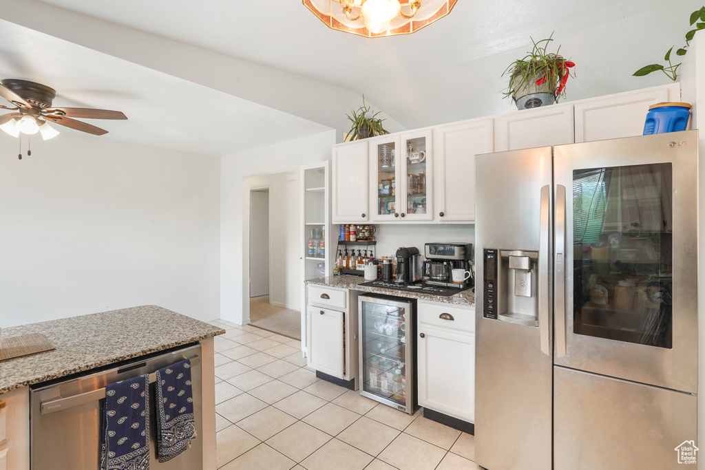 Kitchen with ceiling fan, beverage cooler, white cabinets, light stone counters, and stainless steel appliances