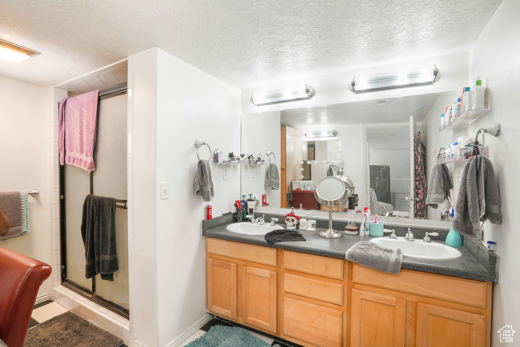 Bathroom featuring double sink vanity, a textured ceiling, and a shower with shower door