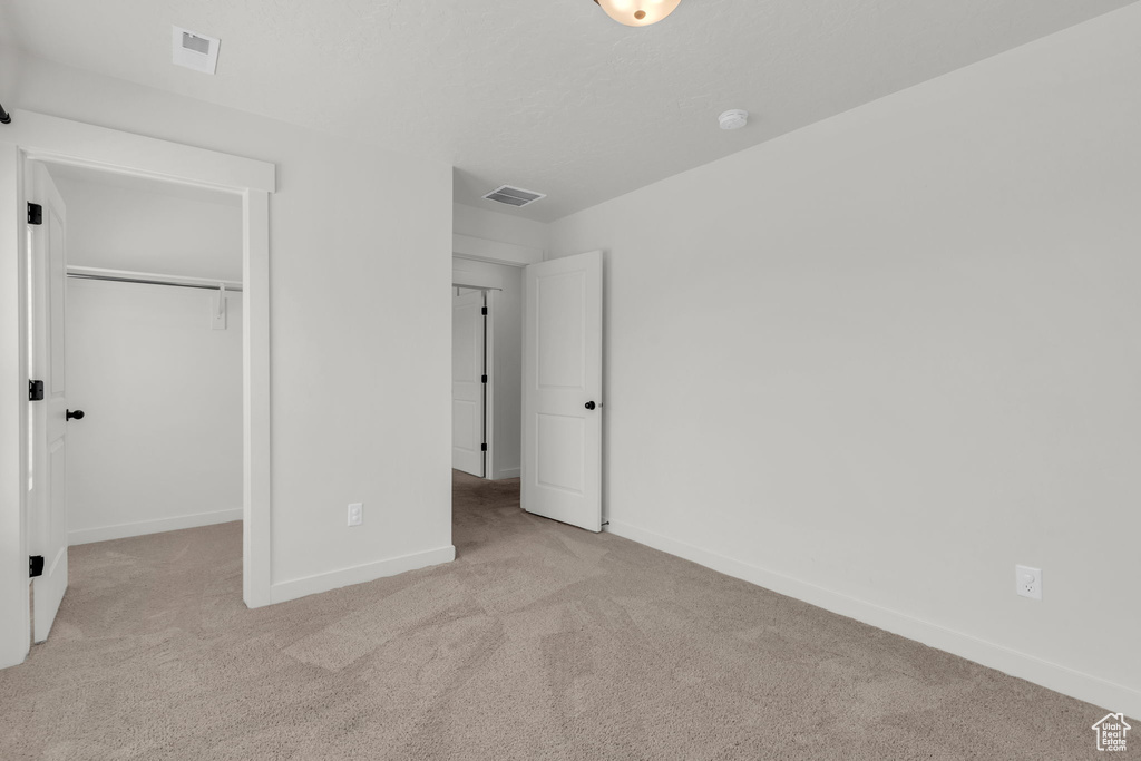 Unfurnished bedroom featuring a spacious closet, light carpet, and a closet