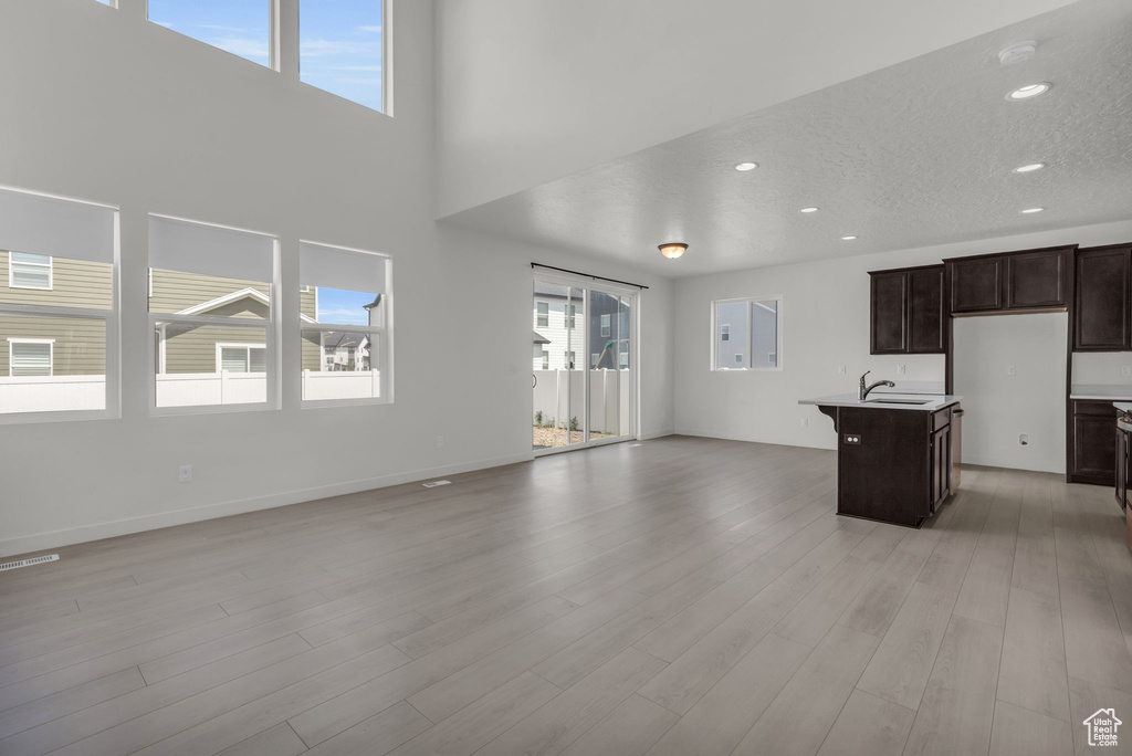 Kitchen featuring a textured ceiling, dark brown cabinets, a center island with sink, sink, and light hardwood / wood-style floors