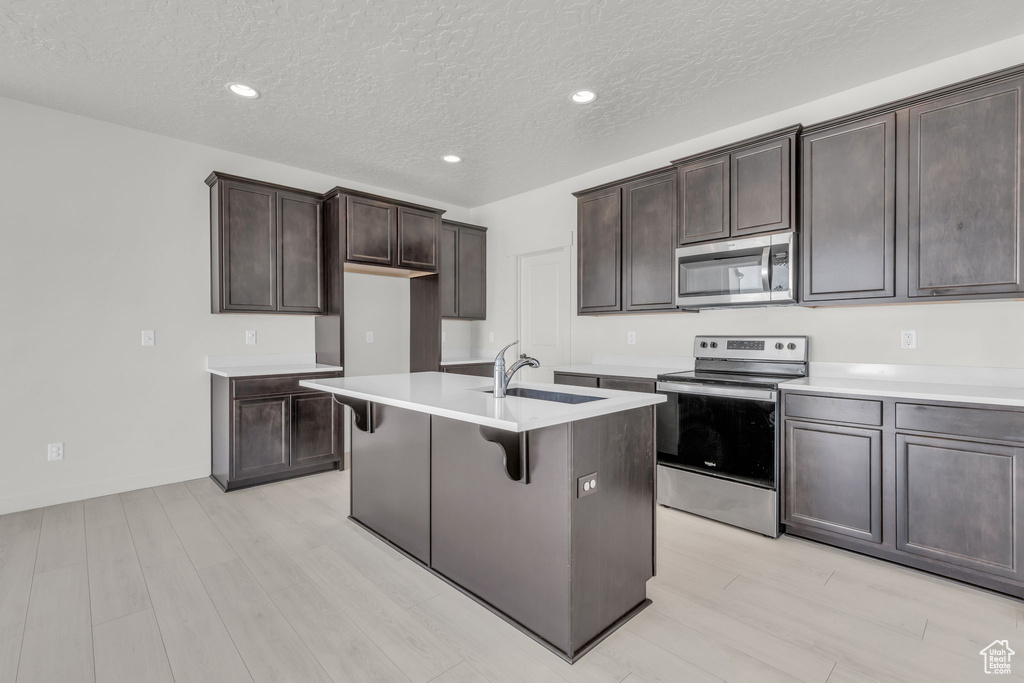 Kitchen with dark brown cabinets, light hardwood / wood-style floors, an island with sink, stainless steel appliances, and sink