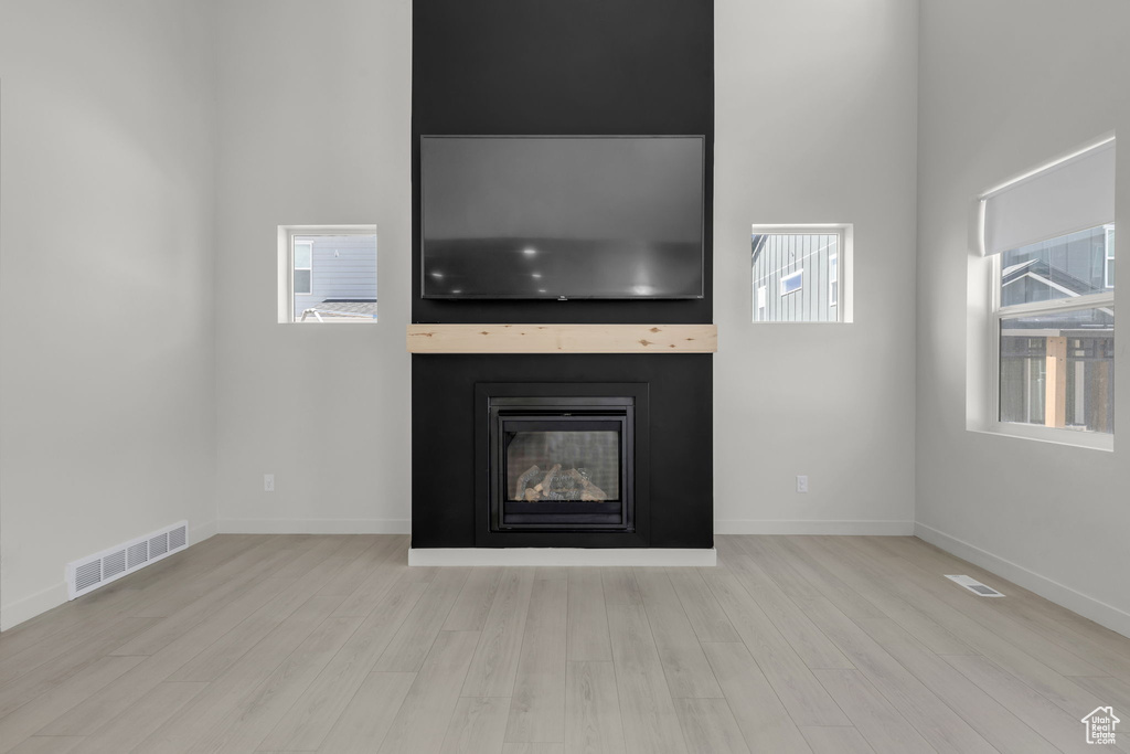 Unfurnished living room with a fireplace, light hardwood / wood-style flooring, and a towering ceiling