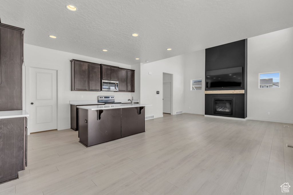 Kitchen with a center island with sink, a fireplace, a kitchen breakfast bar, stainless steel appliances, and light hardwood / wood-style flooring