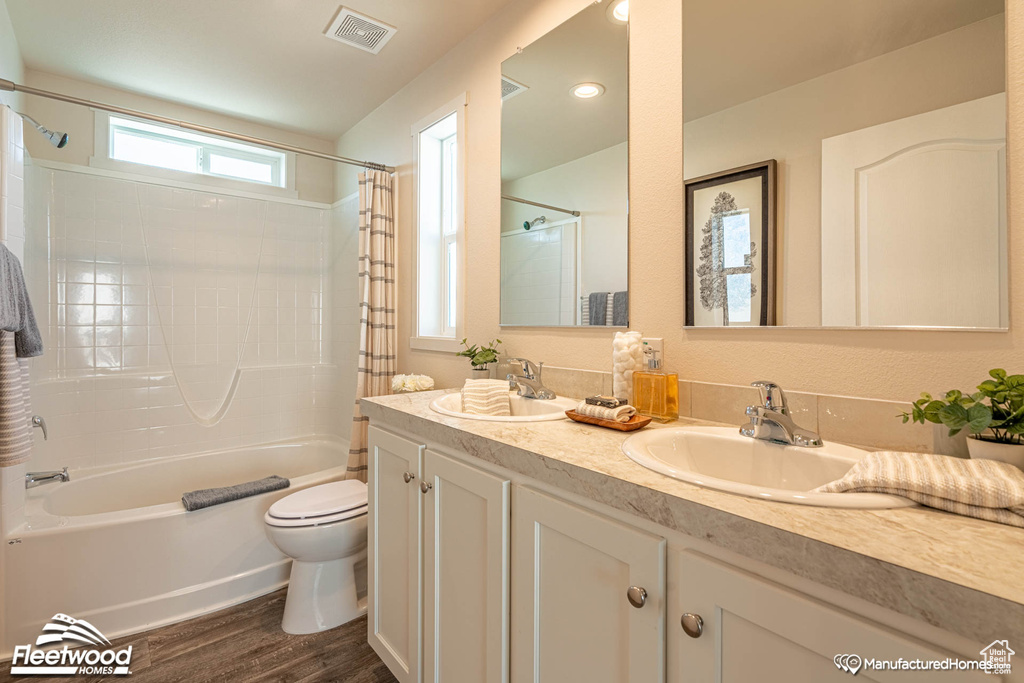 Full bathroom with double sink vanity, toilet, shower / bath combination with curtain, and hardwood / wood-style flooring