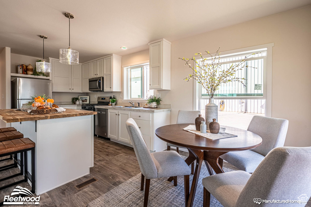 Kitchen with stainless steel appliances, sink, white cabinets, dark wood-type flooring, and butcher block counters