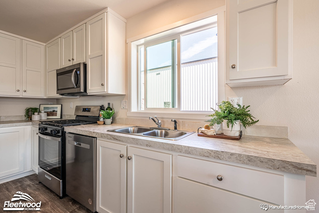 Kitchen featuring appliances with stainless steel finishes, dark hardwood / wood-style flooring, sink, and white cabinets