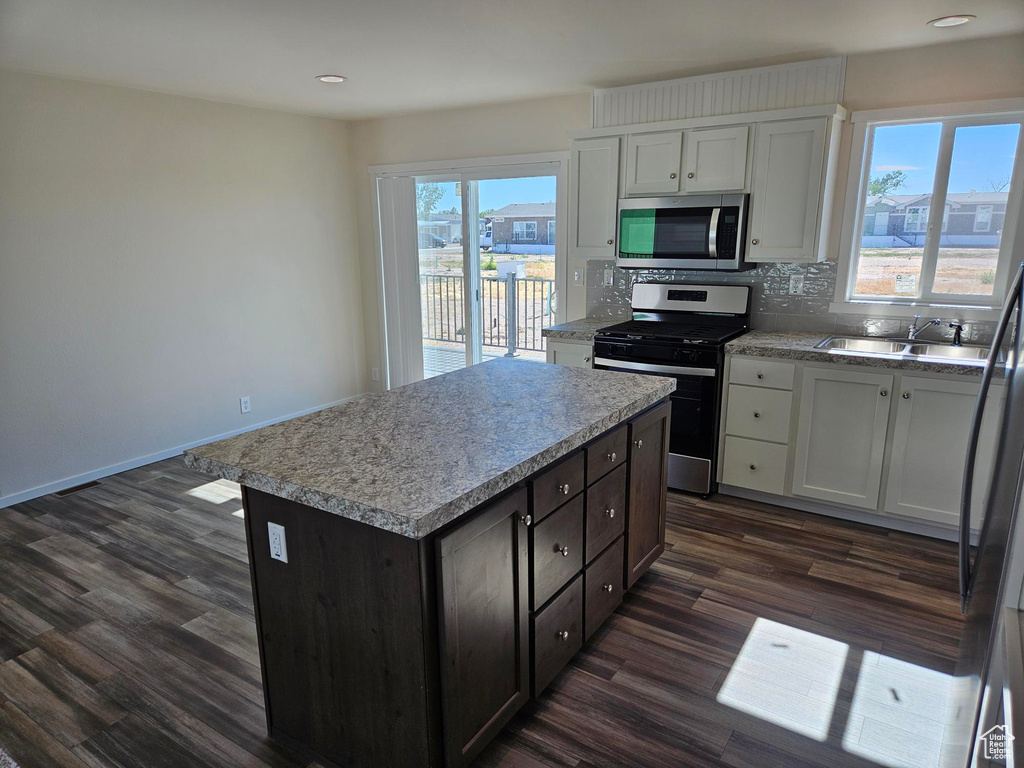 Kitchen with decorative backsplash, appliances with stainless steel finishes, sink, dark wood-type flooring, and a kitchen island