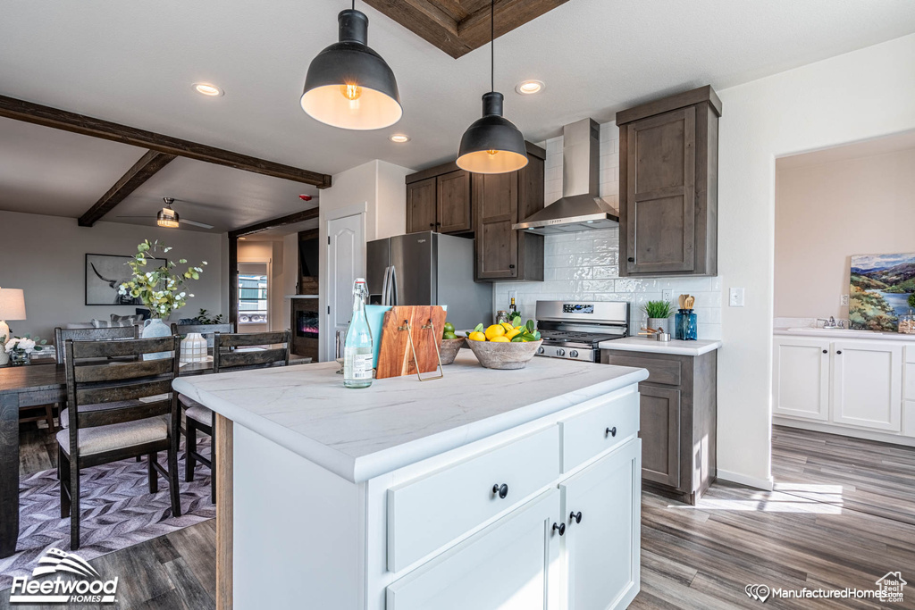 Kitchen with appliances with stainless steel finishes, white cabinetry, beamed ceiling, wall chimney range hood, and hardwood / wood-style floors