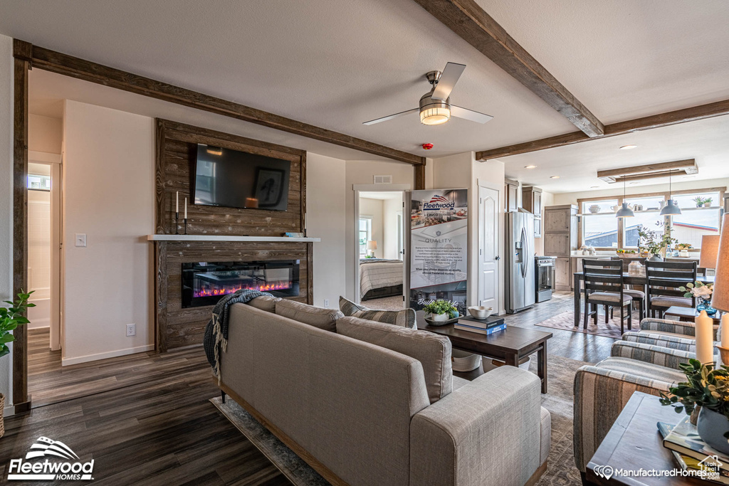 Living room with a large fireplace, beam ceiling, hardwood / wood-style floors, and ceiling fan