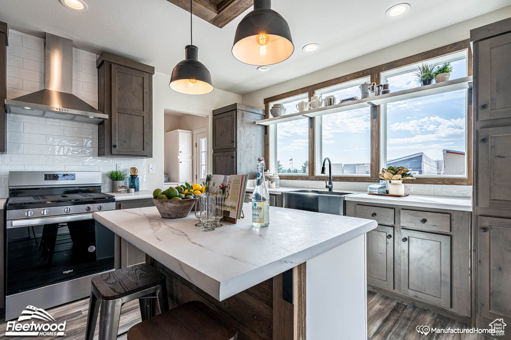 Kitchen featuring gas stove, sink, wall chimney exhaust hood, backsplash, and dark hardwood / wood-style flooring