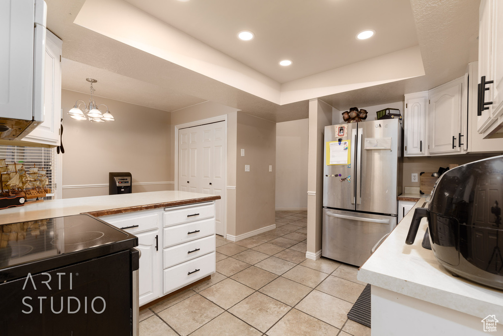 Kitchen featuring white cabinets, pendant lighting, stainless steel fridge, light tile patterned floors, and a tray ceiling