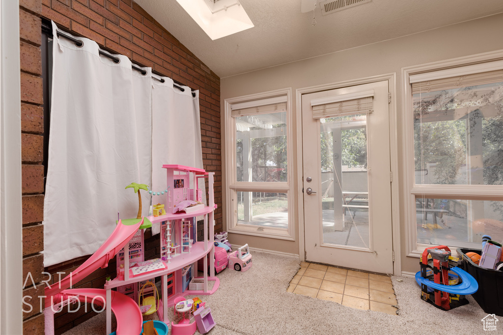 Playroom with carpet flooring, plenty of natural light, vaulted ceiling with skylight, and brick wall