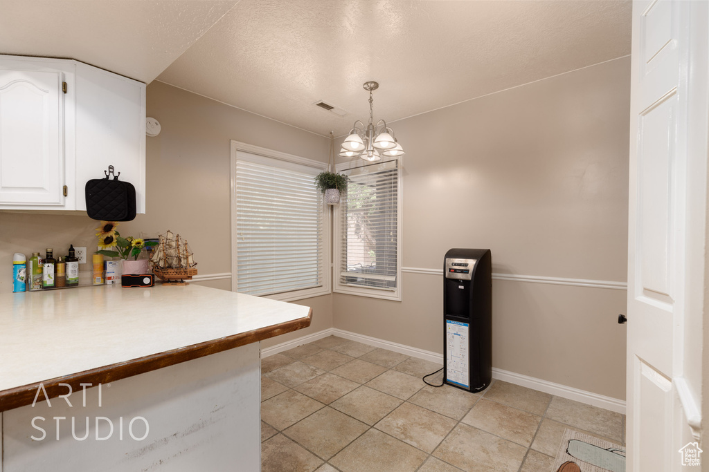 Kitchen with light tile patterned flooring, decorative light fixtures, white cabinetry, and an inviting chandelier