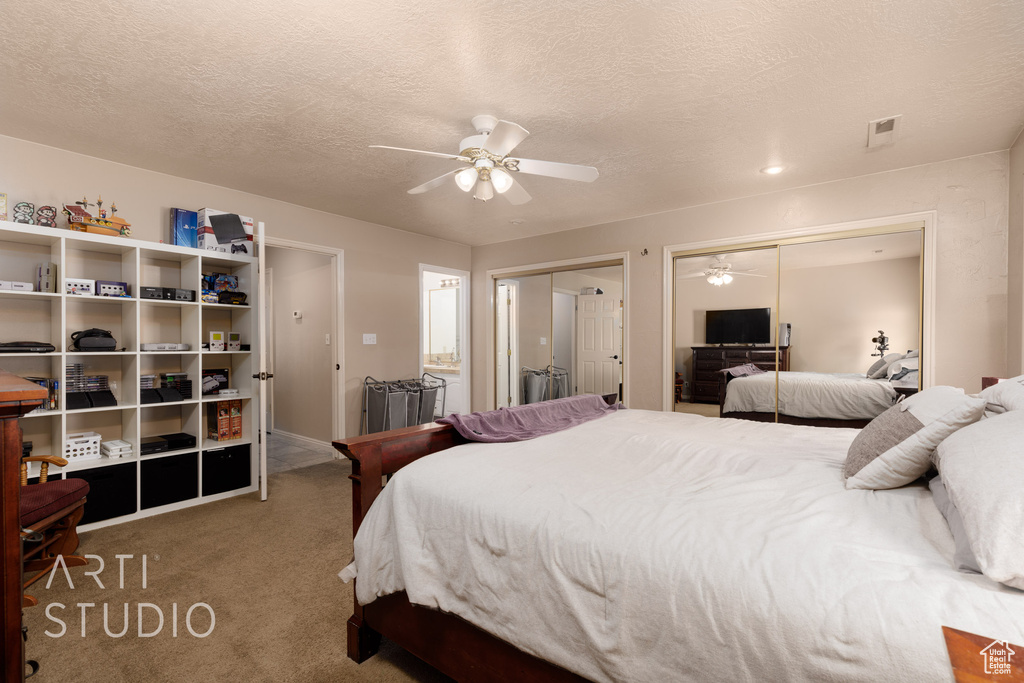 Carpeted bedroom featuring a textured ceiling, two closets, and ceiling fan