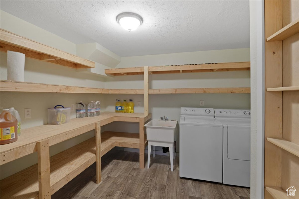 Clothes washing area with washer and clothes dryer, a textured ceiling, and hardwood / wood-style floors