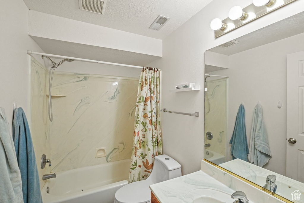 Full bathroom featuring a textured ceiling, shower / bath combo with shower curtain, toilet, and vanity