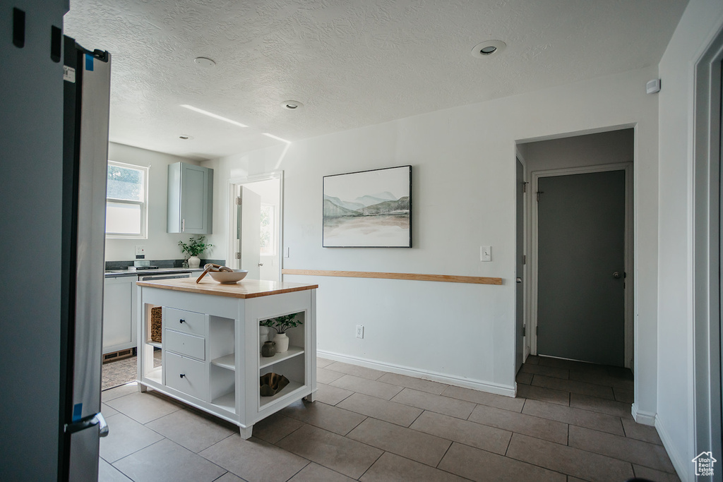 Interior space featuring stainless steel fridge, a textured ceiling, light tile patterned floors, and white cabinetry