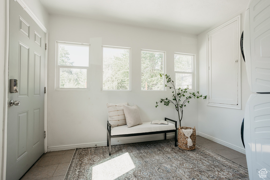 Living area featuring stacked washer and dryer, light tile patterned floors, and a healthy amount of sunlight