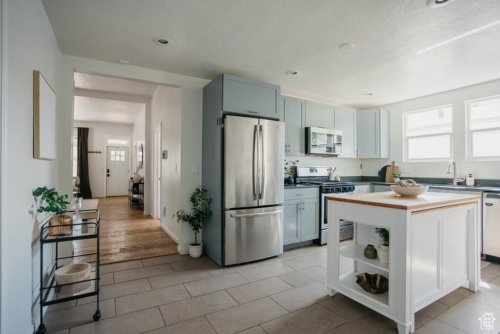 Kitchen featuring a textured ceiling, stainless steel appliances, light hardwood / wood-style floors, a center island, and sink