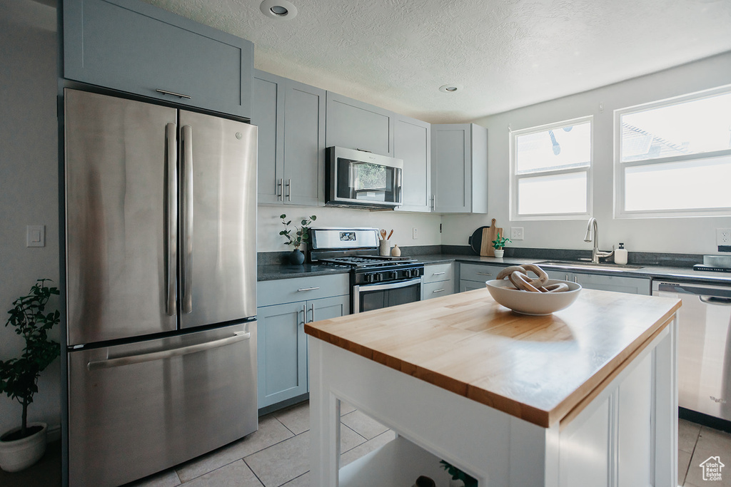 Kitchen featuring appliances with stainless steel finishes, a kitchen island, gray cabinets, sink, and light tile patterned flooring