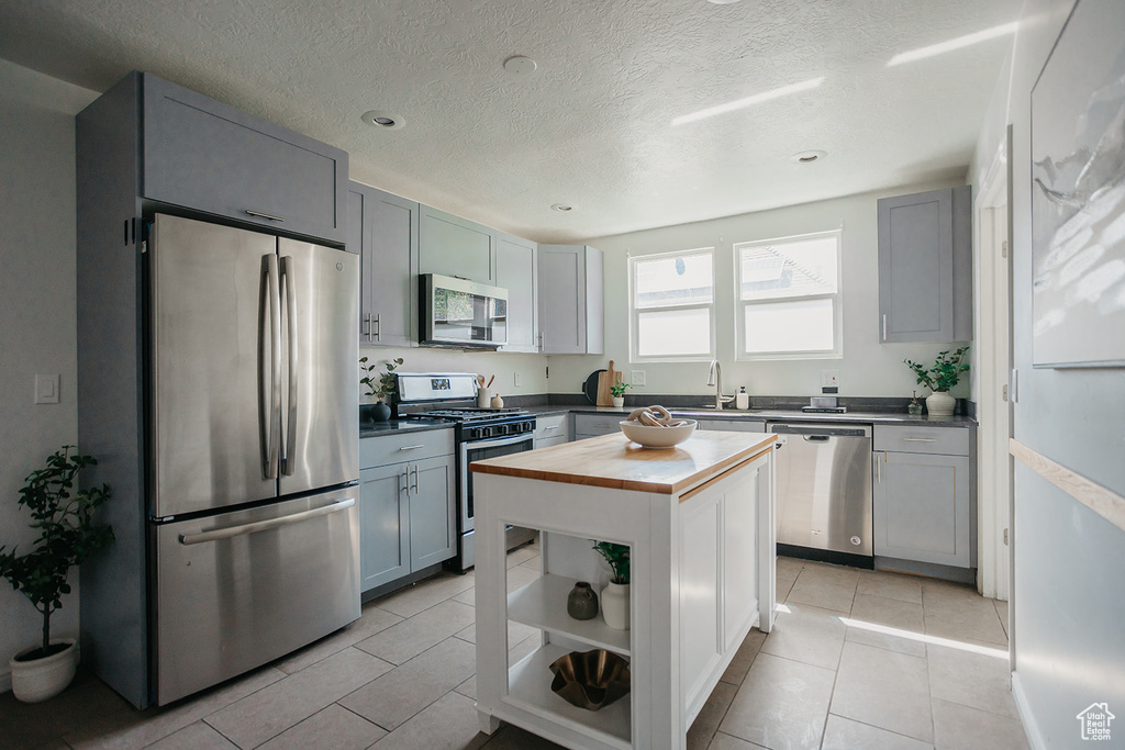 Kitchen with gray cabinets, light tile patterned floors, stainless steel appliances, a kitchen island, and butcher block counters