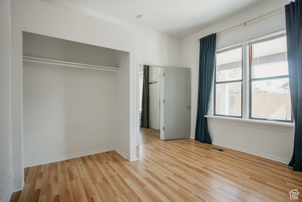 Unfurnished bedroom featuring light hardwood / wood-style flooring, multiple windows, and a closet