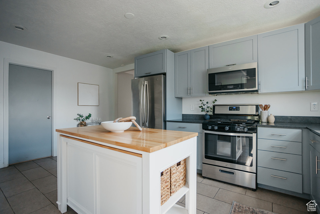 Kitchen featuring appliances with stainless steel finishes, gray cabinets, light tile patterned floors, and butcher block counters