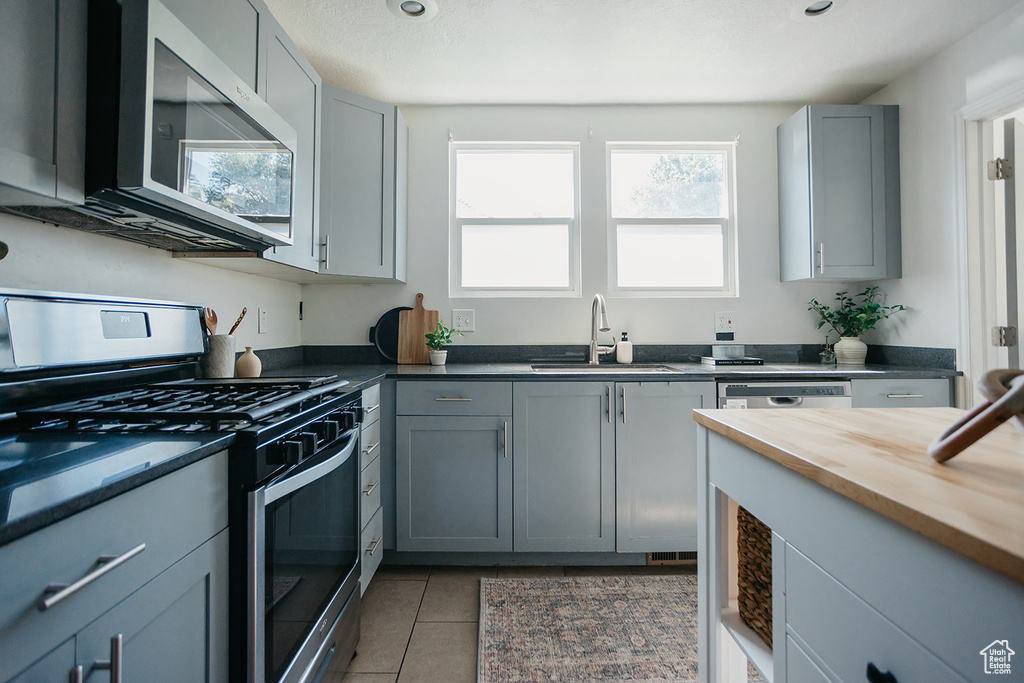 Kitchen featuring sink, stainless steel appliances, light tile patterned floors, and gray cabinetry