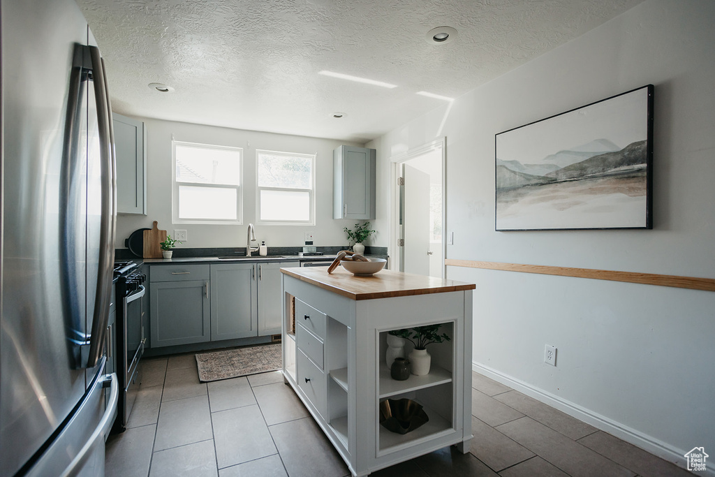 Kitchen with a textured ceiling, gray cabinets, wood counters, stainless steel appliances, and sink