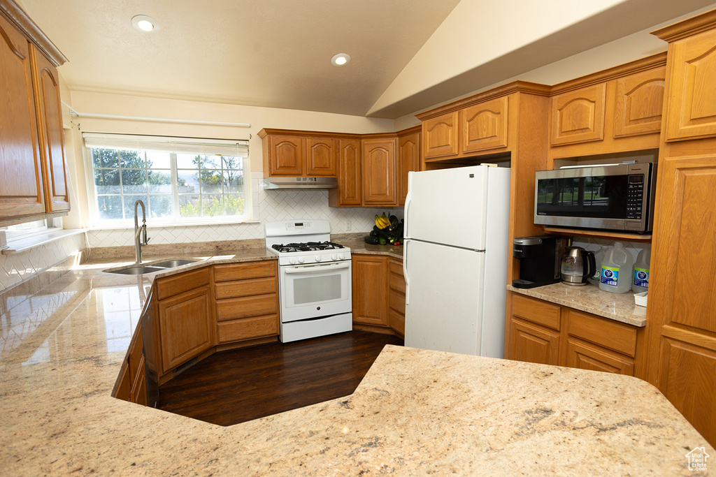 Kitchen featuring backsplash, vaulted ceiling, sink, white appliances, and dark wood-type flooring