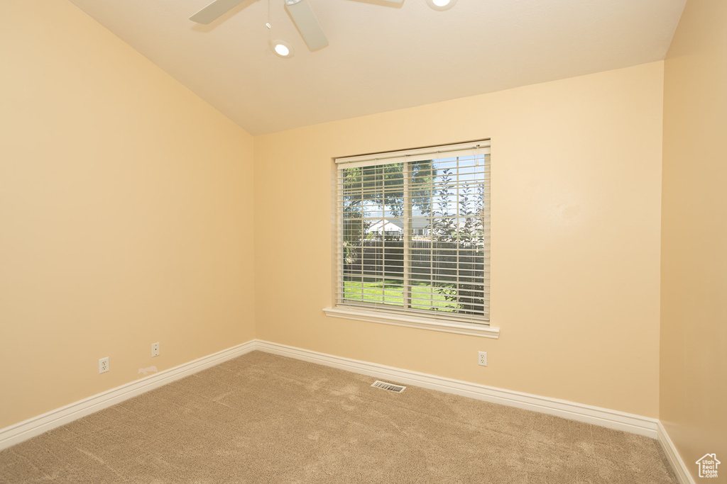 Empty room with ceiling fan, vaulted ceiling, and carpet floors