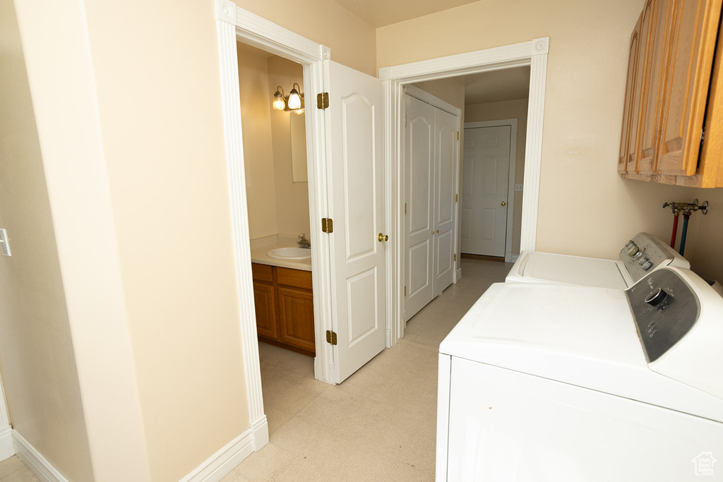 Laundry area featuring washer and dryer, light tile patterned floors, sink, and cabinets