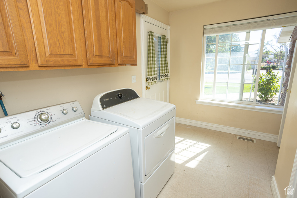 Clothes washing area featuring washer and clothes dryer, cabinets, and light tile patterned floors