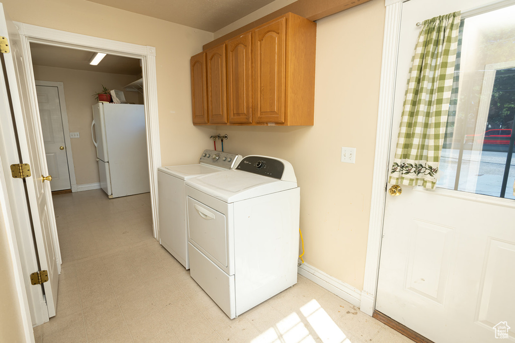 Clothes washing area with light tile patterned floors, independent washer and dryer, and cabinets